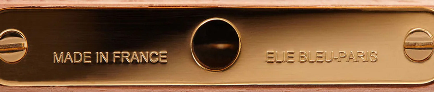 Close-up of a metallic plate with engraved text: "MADE IN FRANCE" on the left and "ELIE BLEU PARIS" on the right, flanking a central circular screw.
