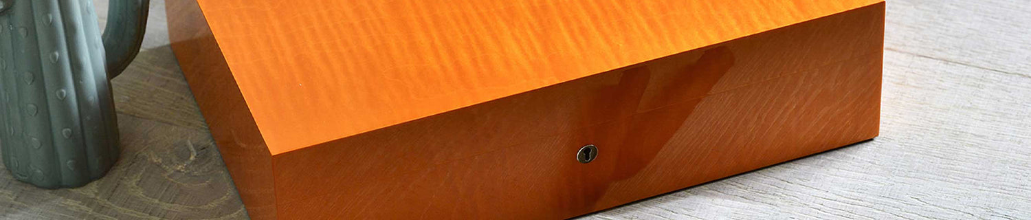 A glossy wooden box with a keyhole rests on a wooden surface. A green vase is partially visible on the side.