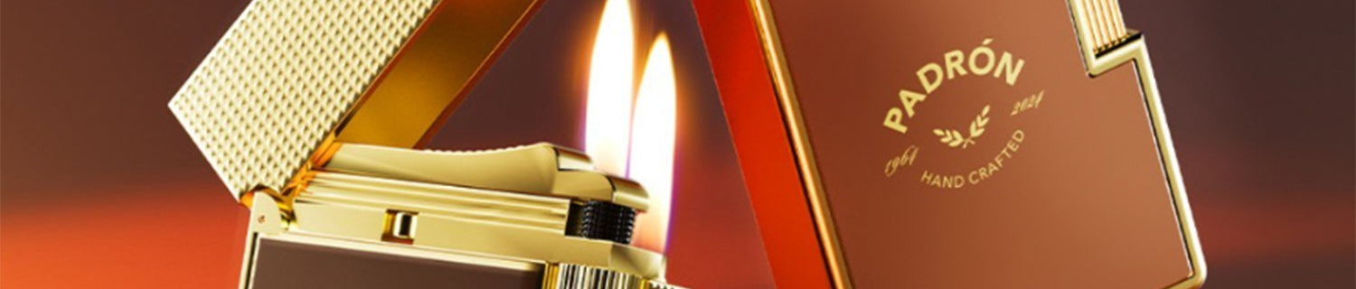 A gold lighter with the lid open, producing a flame. The lighter is embossed with "Padron Handcrafted.