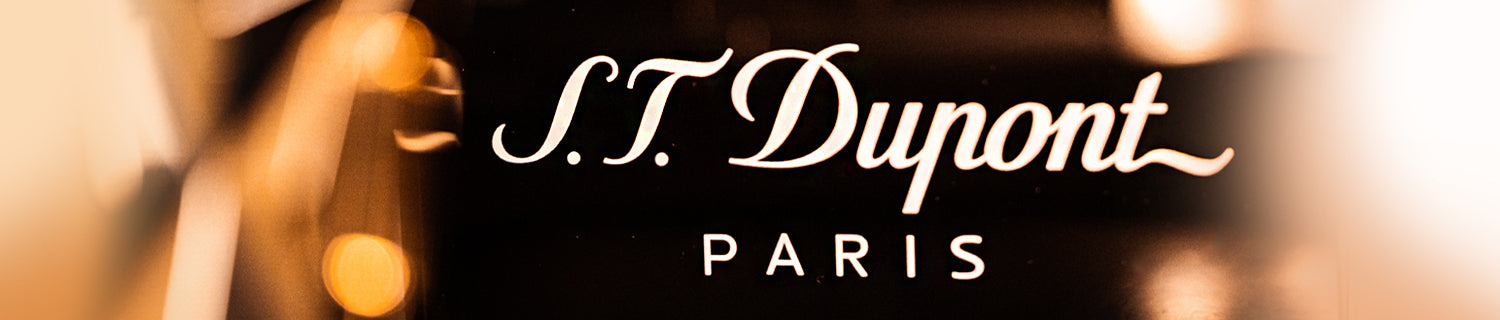 S.T. Dupont Paris logo in stylized white script on a dark, blurred background.