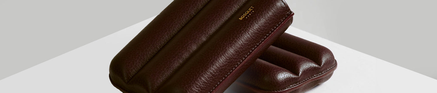 Close-up of a brown leather pouch with embossed text, placed on a white surface against a light gray background.