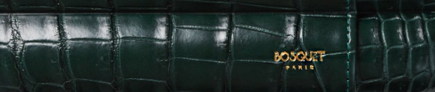 Close-up of a dark green crocodile-patterned leather surface with gold embossed text "BOSQUET PARIS.