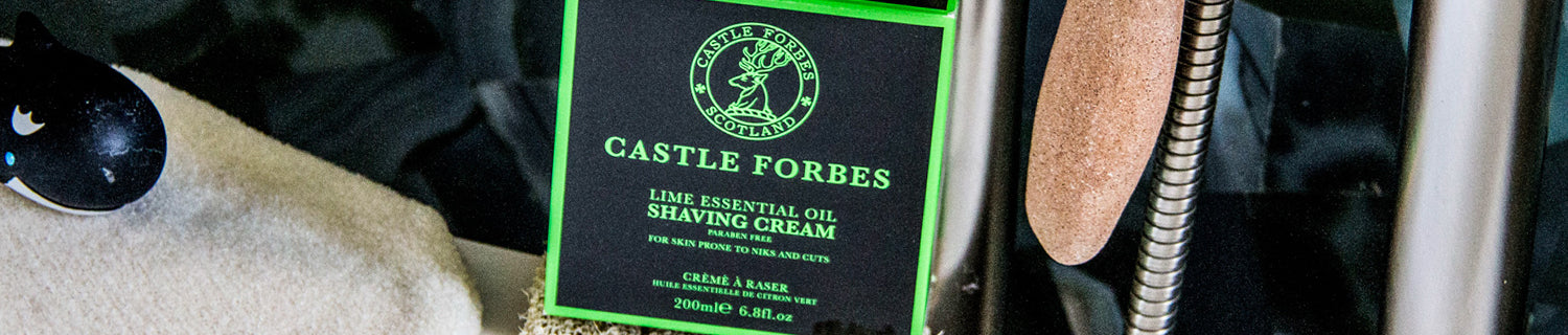 Box of Castle Forbes Lime Essential Oil Shaving Cream with black and green design next to a soft cloth and a metal spring.