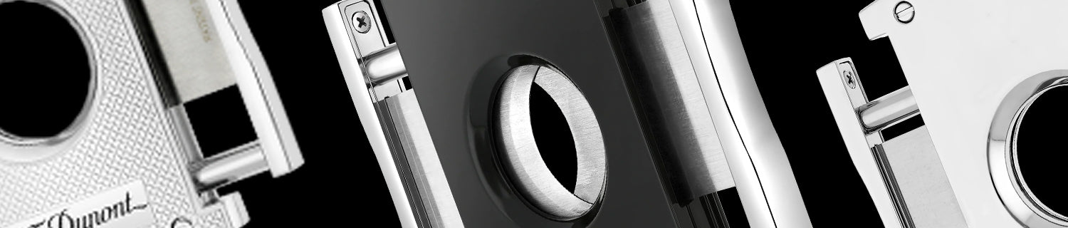 Close-up of three metallic cigar cutters with various textures and designs on a black background.