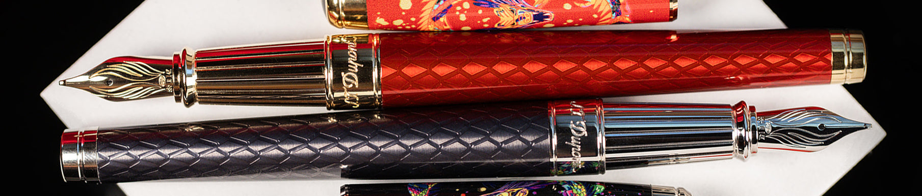 Three ornate fountain pens with intricate designs, featuring gold nibs and colorful patterns, are displayed on a white surface.