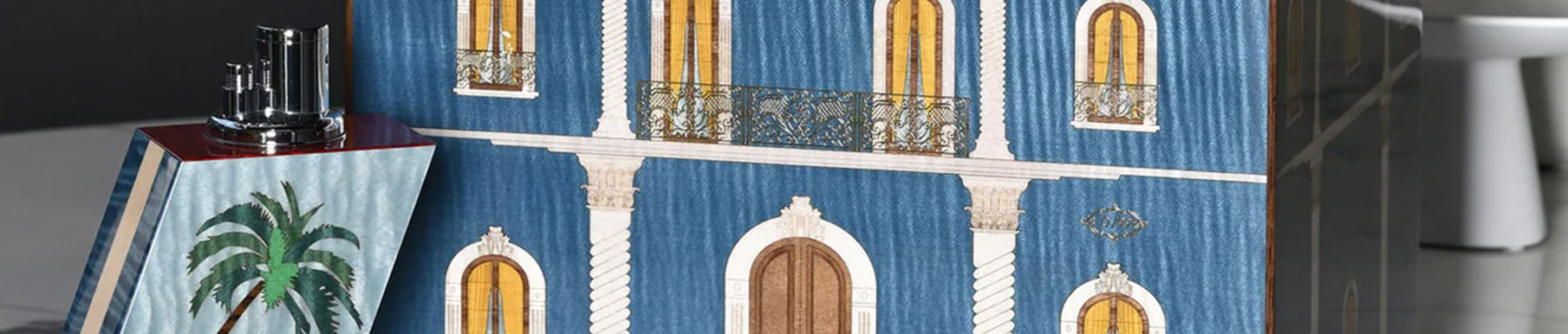 Elegant blue building facade with arched windows and ornate balconies; palm tree artwork on a nearby object in the foreground.