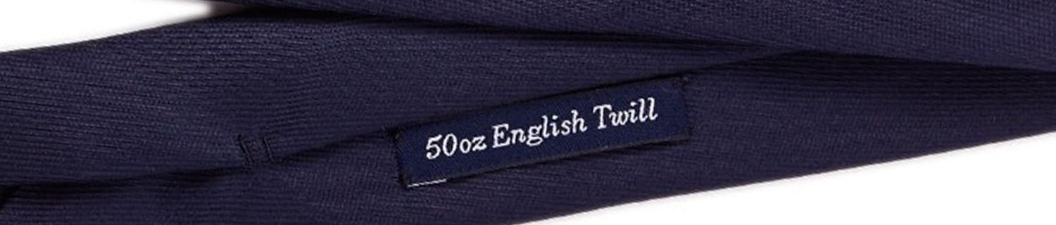 Close-up of a fabric with a label reading "50oz English Twill" in white text on a dark background. The fabric appears to be dark-colored and textured.