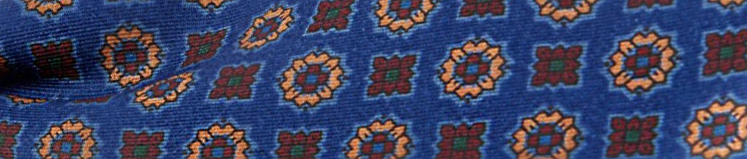 Close-up of a blue fabric with an orange and red geometric floral pattern.