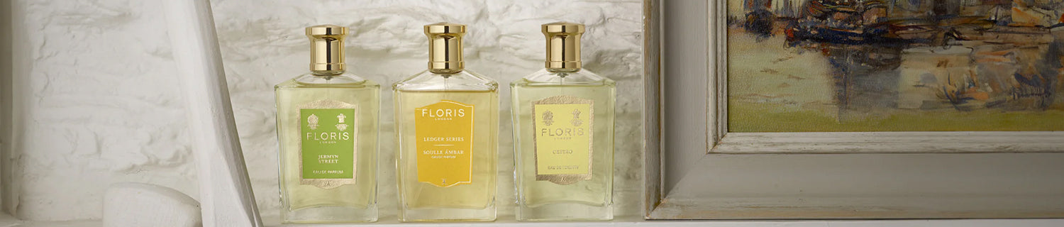 Three perfume bottles with Floris labels, placed on a shelf next to a framed painting.