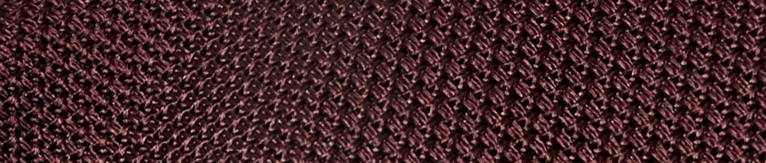 Close-up of a textured, woven pattern in dark brown and maroon hues, resembling a tightly braided fabric or netting.