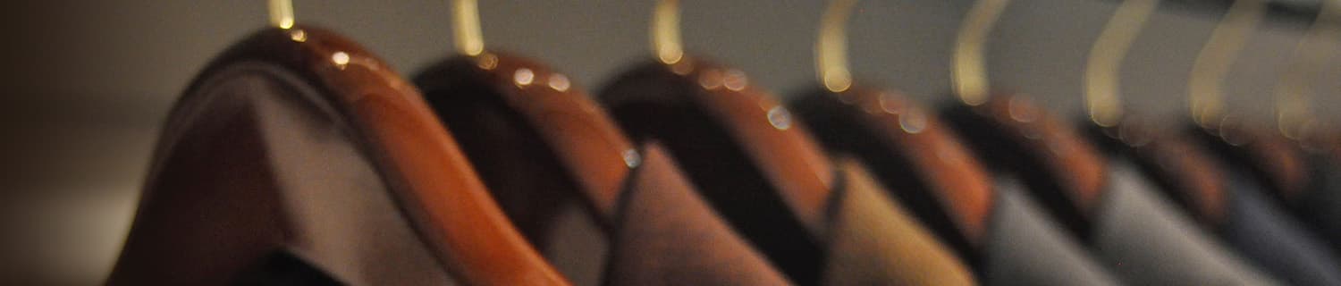 Close-up of wooden hangers holding various suits in a row, with a blurred background.