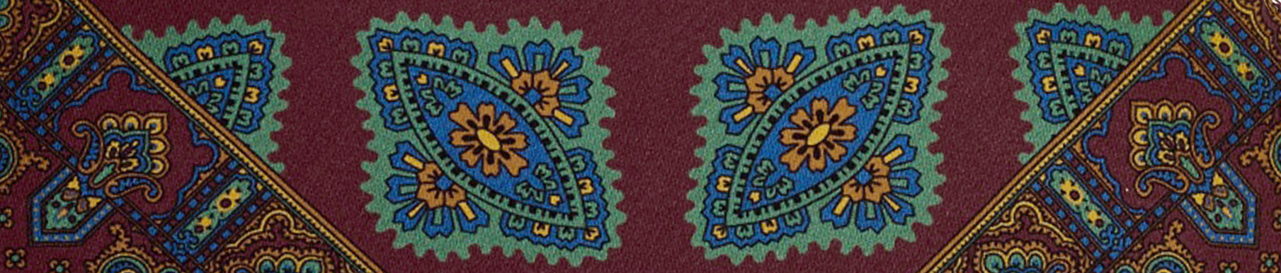 A patterned textile featuring blue, green, and yellow geometric floral designs on a maroon background.