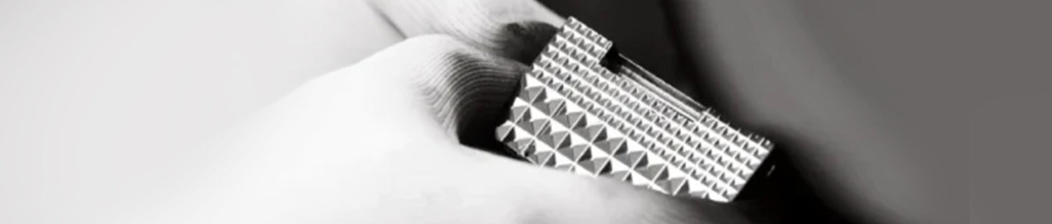 A hand holding a rectangular, metallic object with a geometric, pyramid-like textured surface.