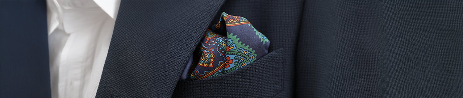 A close-up of a dark textured suit jacket with a colorful paisley pocket square neatly tucked into the breast pocket.