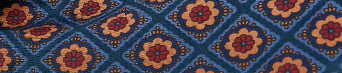 Geometric fabric pattern with blue diamond shapes and red floral centers, surrounded by beige motifs.
