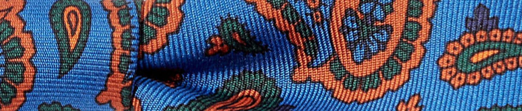 Close-up of blue fabric with an orange and green paisley pattern, showing a slight fold in the material.