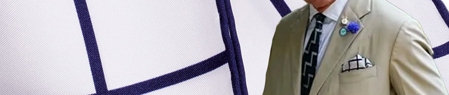 A person wearing a light beige suit with a patterned tie and pocket square, standing against a background with a blue and white checkered pattern.