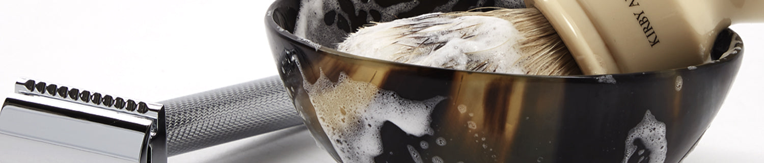 Shaving brush in a bowl with lather, next to a safety razor.