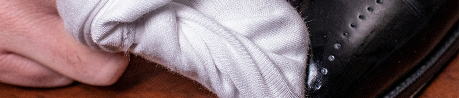 A hand is polishing a black shoe with a white cloth, focusing on the toe area.
