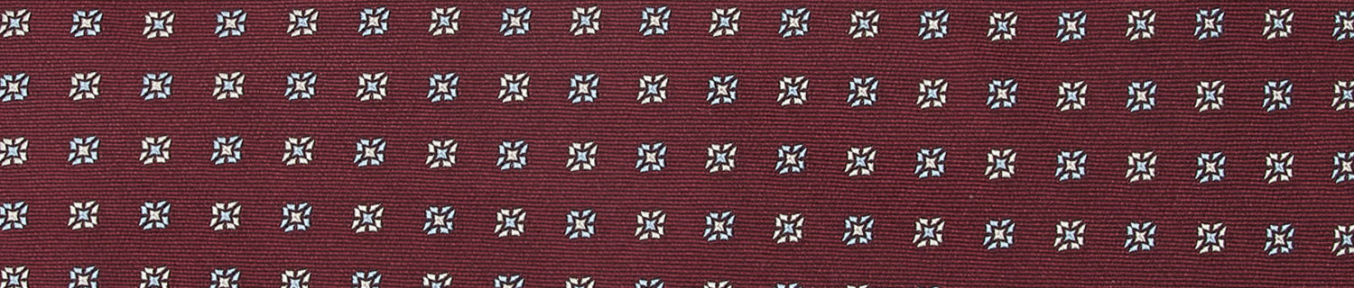 Patterned fabric in maroon with rows of small, white and blue geometric designs.