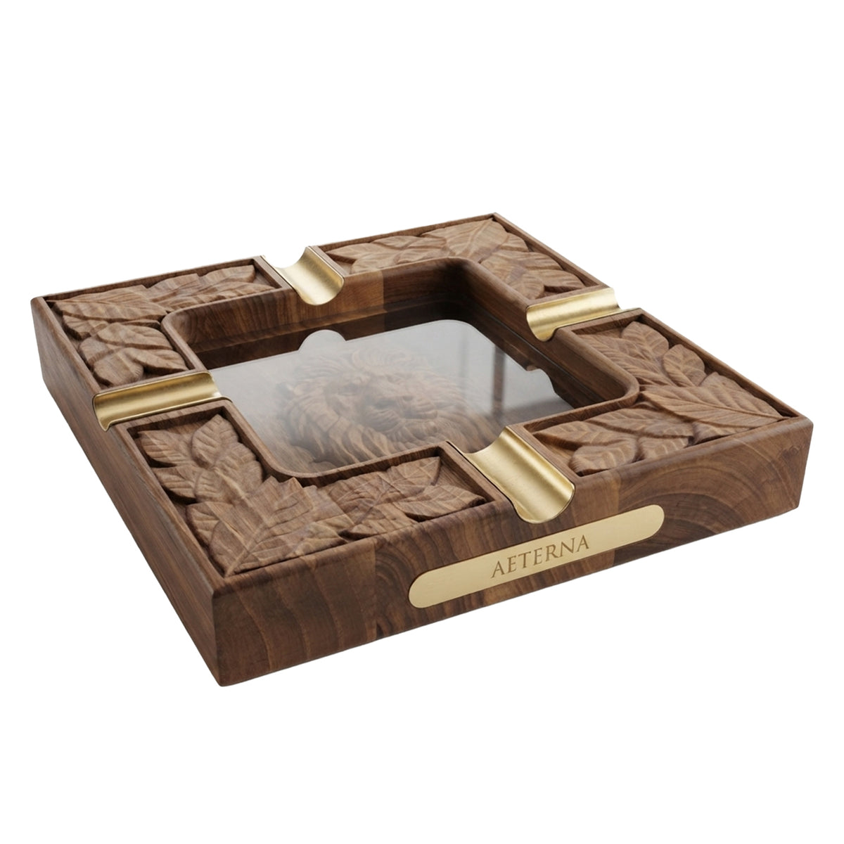 A square carved wooden ashtray featuring a detailed lion head in the center with a layer of glass over it and leaf motifs around the border, accented with gold-toned metal dividers.