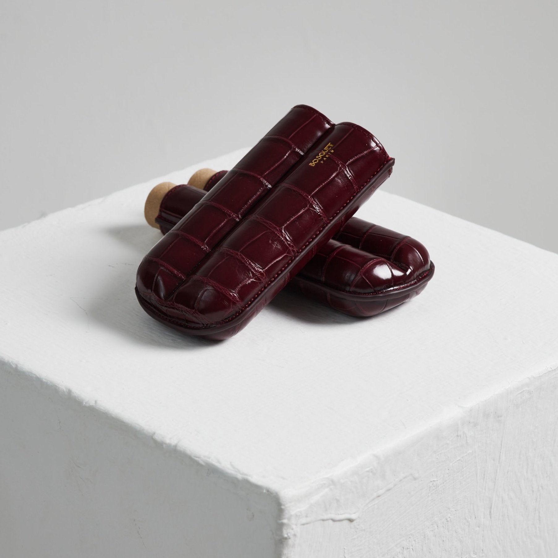 A pair of Bosquet Crocodile Cigar Case, Burgundy ice cream cups on top of a white cube showcasing Bosque crocodile leathers.