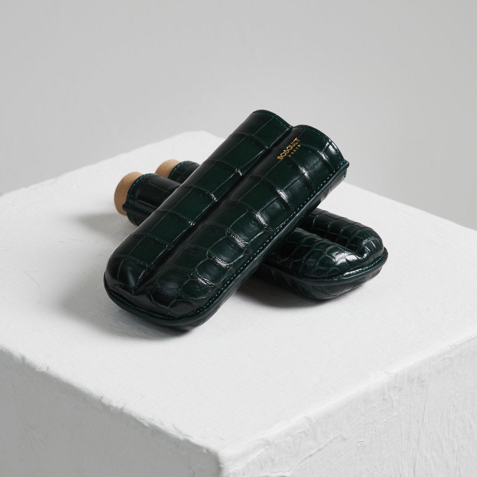 Two Bosque Bosquet Crocodile Cigar Case, Forest Green cases made of green crocodile leather are displayed on top of a white cube.