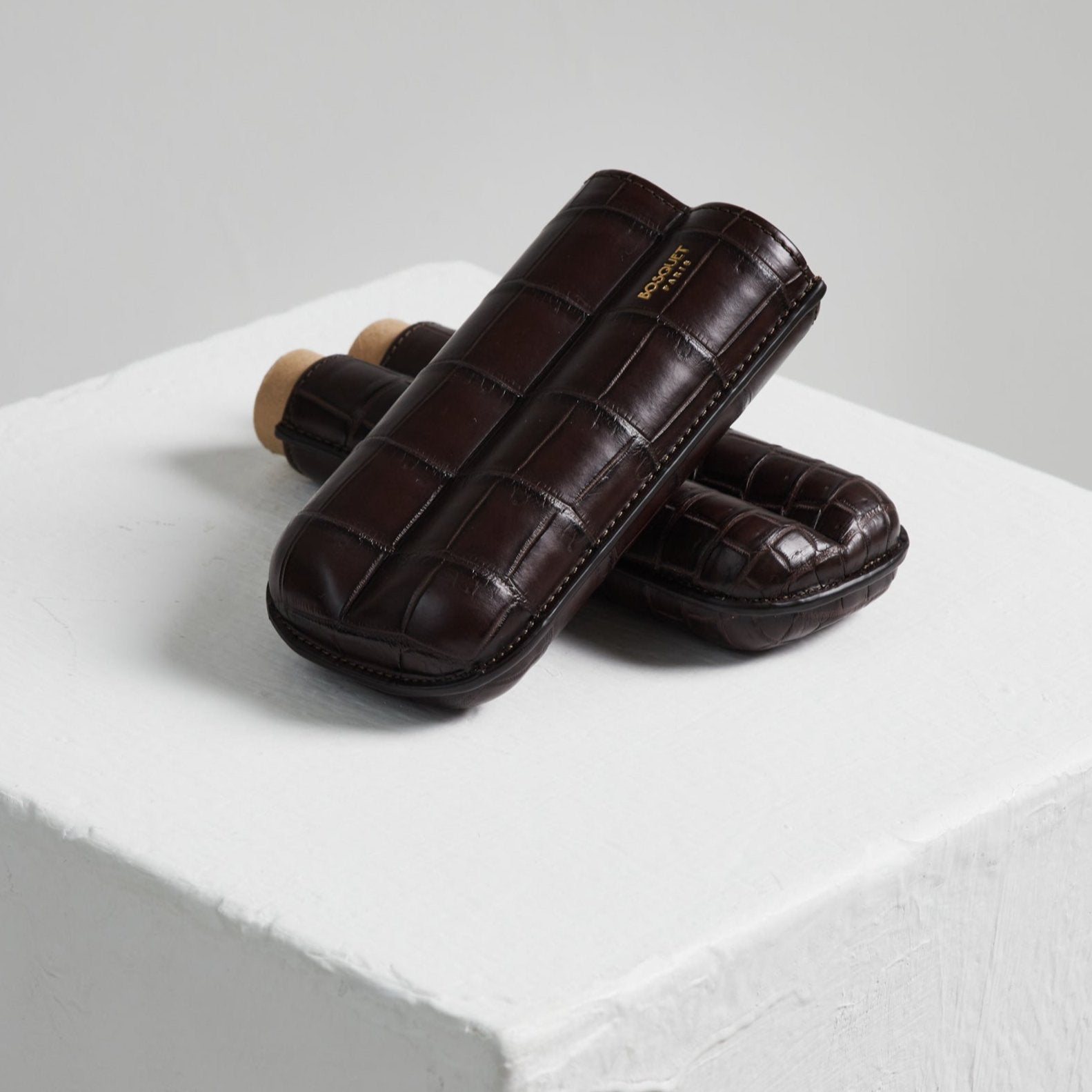 A pair of brown leather Bosque Crocodile cigar cases on a white cube.