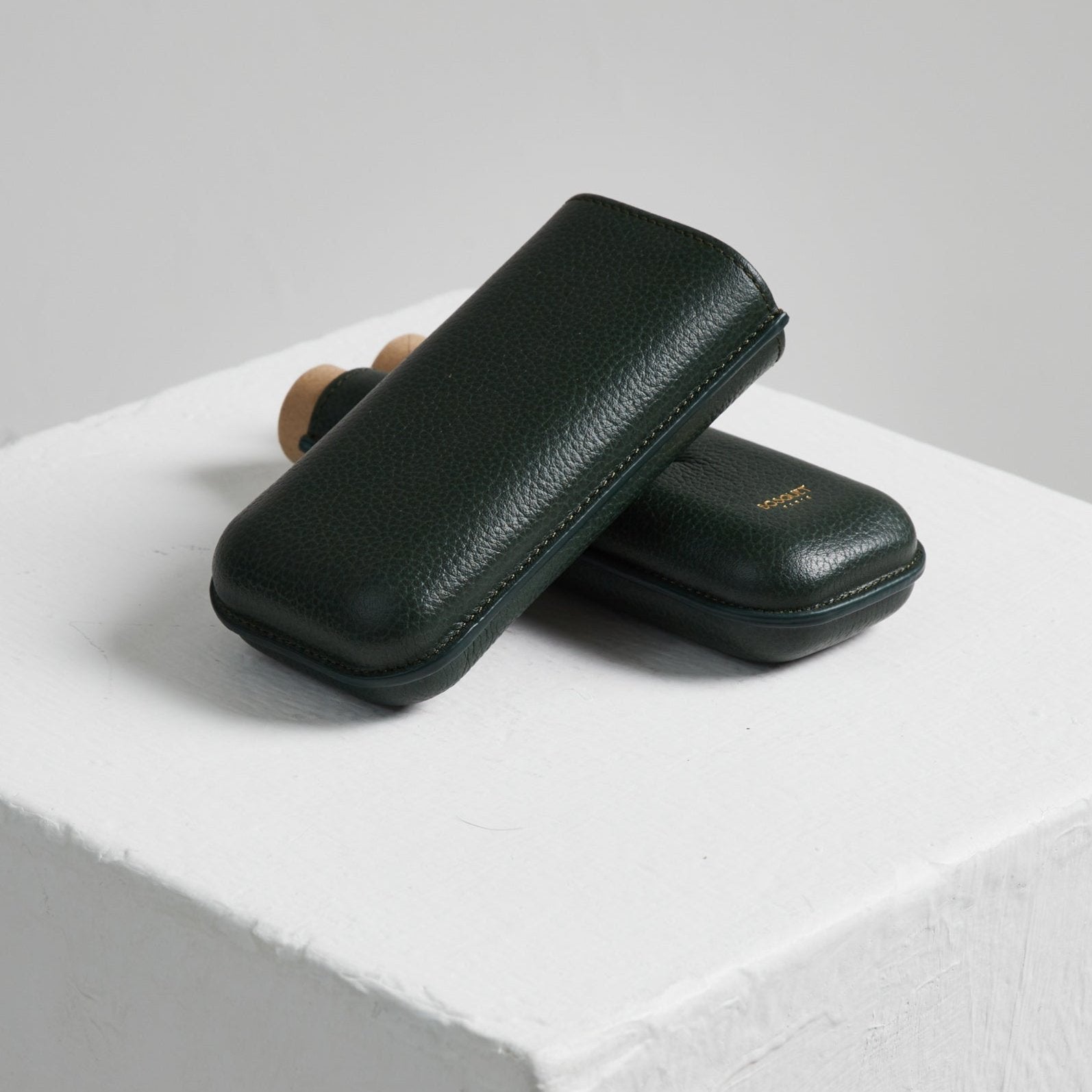 Two green leather Bosque Smooth Forest Green Leather Cigar Cases on top of a white cube.