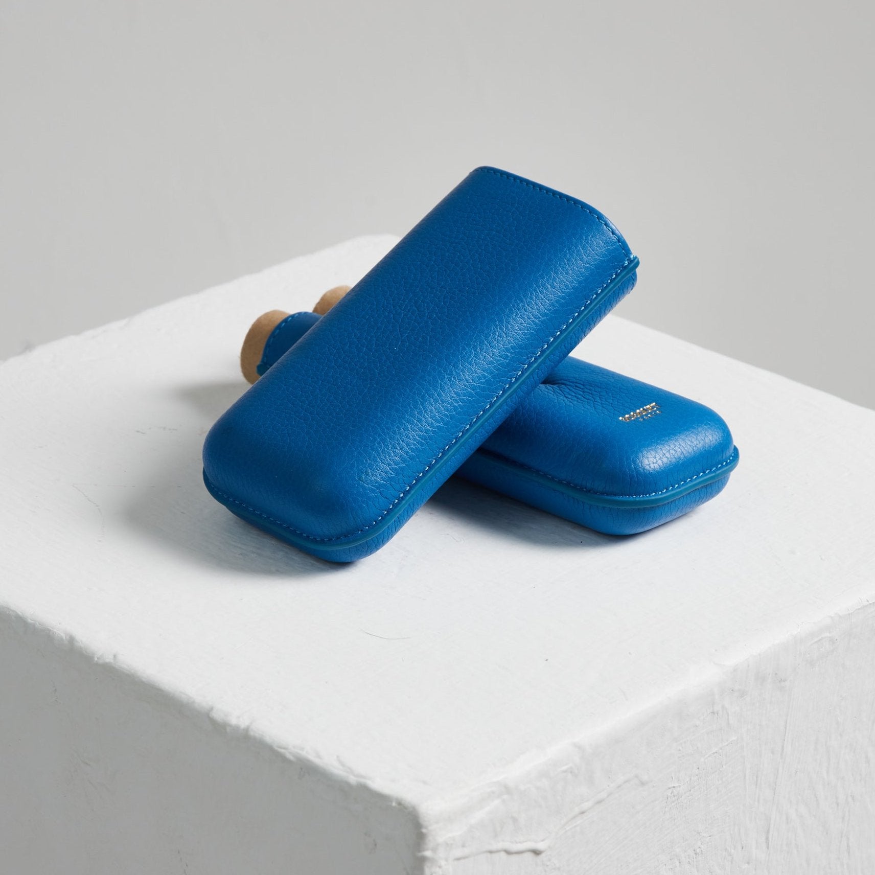 Two blue Bosque Smooth Capri Blue Leather Cigar Cases sitting on top of a white cube.