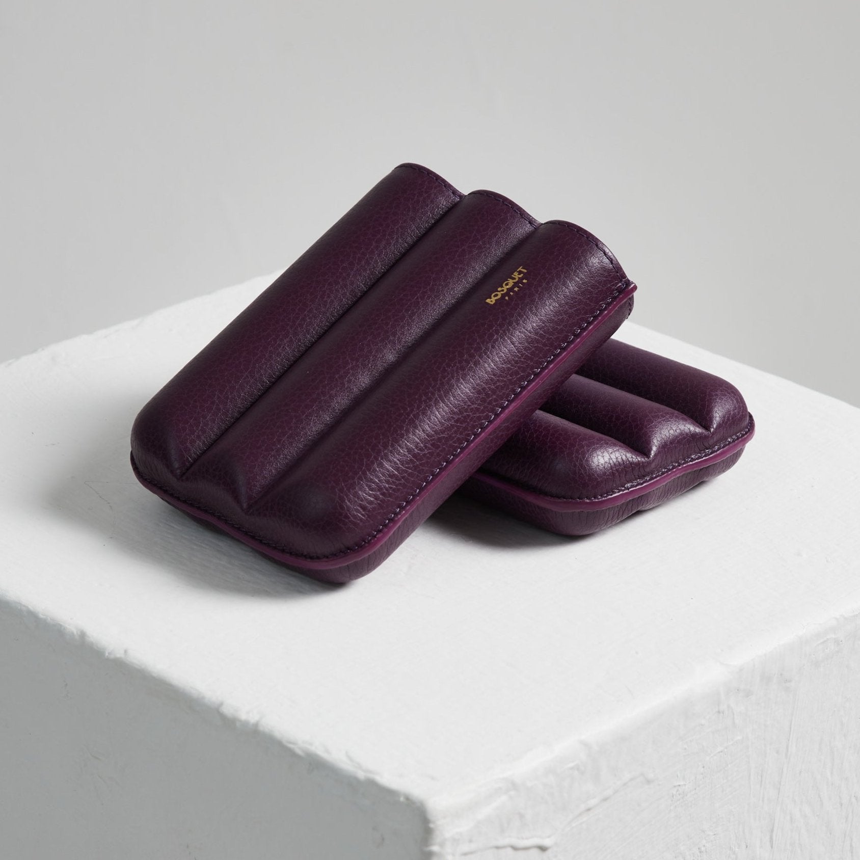 Two Bosque Smooth Purple Cylindrical Leather Cigar Cases sitting on top of a white cube.