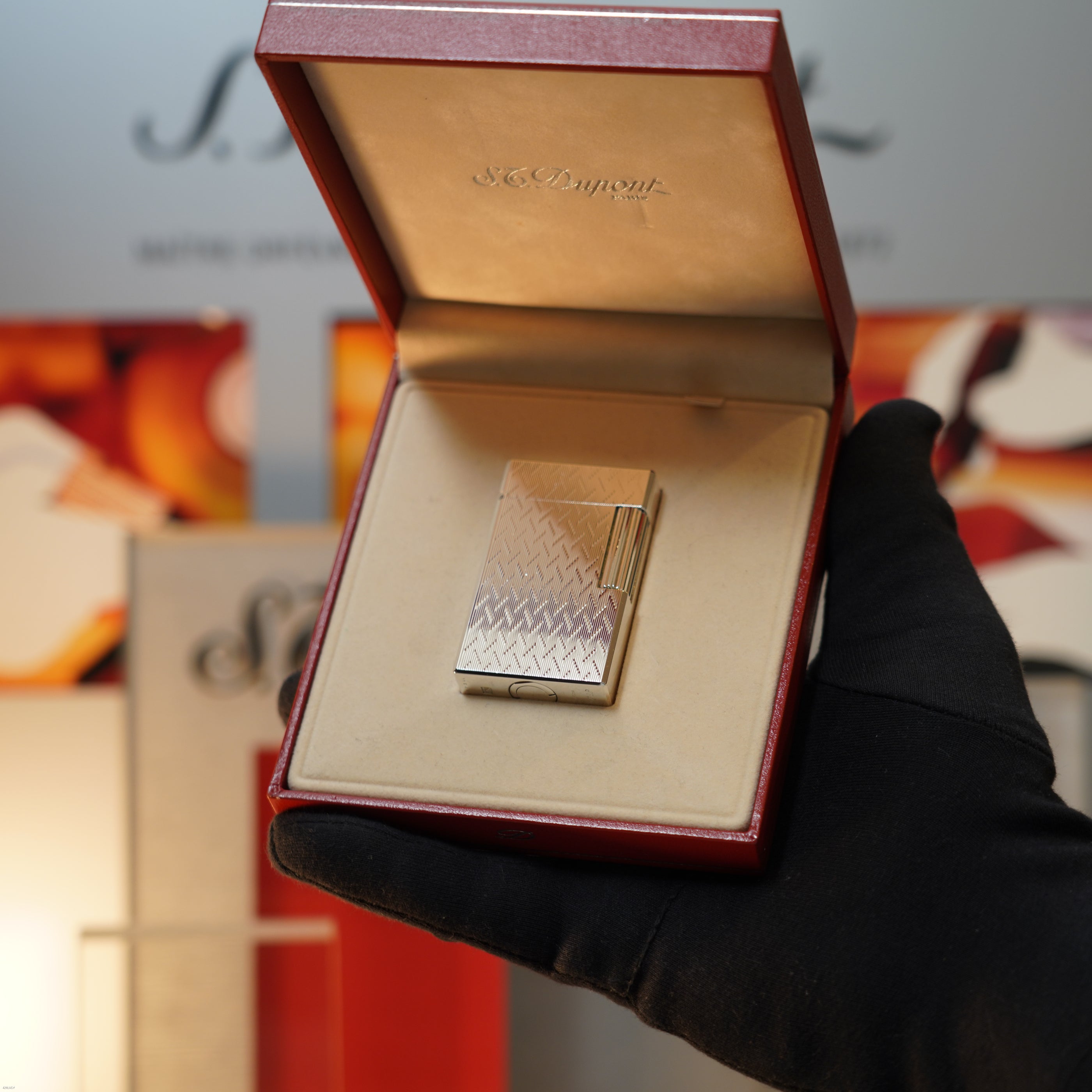 A gloved hand holds an open red box displaying a Lucy Lighter Vintage 1990 S.T. Dupont Ligne 1 Large Herringbone Guilloché Heavy Silver Finish Lighter.