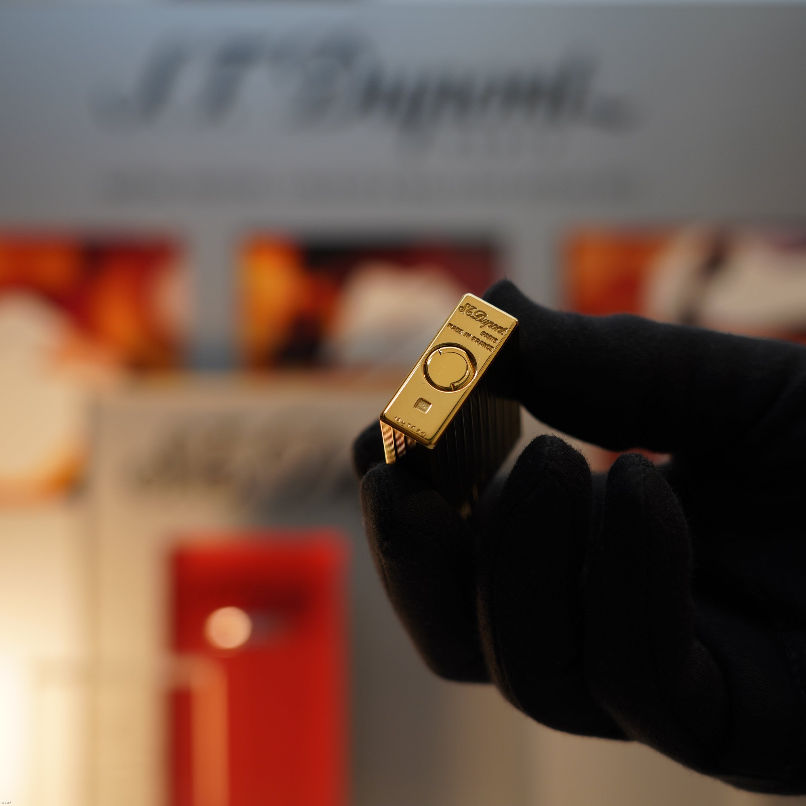A gloved hand holds a Vintage November 1987 S.T. Dupont Large Ligne 1 Heavy rare pattern 18k Gold Finish Lighter by Lucy Lighter, its branding subtly blurred against a vibrant background.