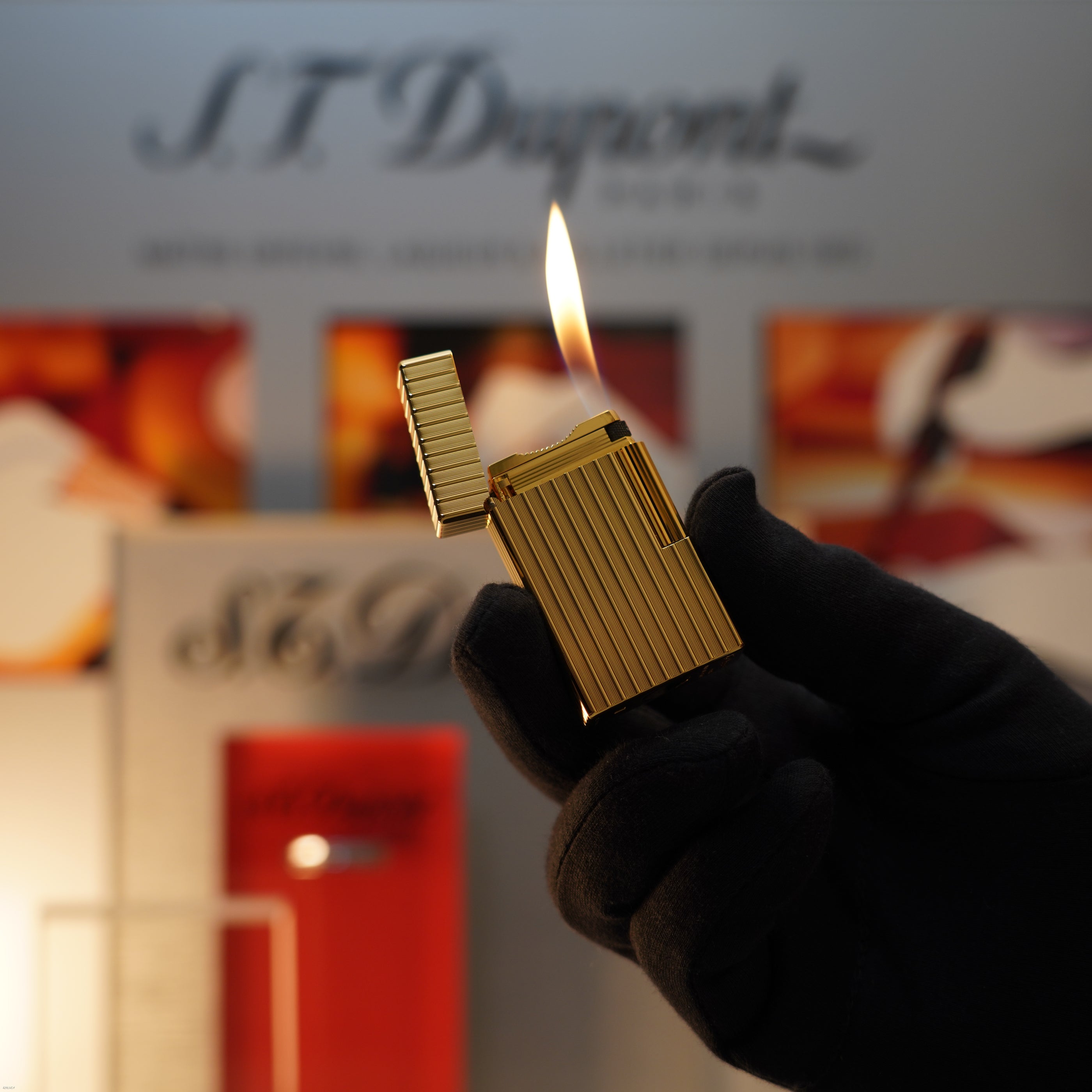 A gloved hand holds a Vintage November 1987 Lucy Lighter S.T. Dupont Large Ligne 1 Heavy rare pattern lighter with an 18k gold finish, set against a blurred S.T. Dupont display backdrop.