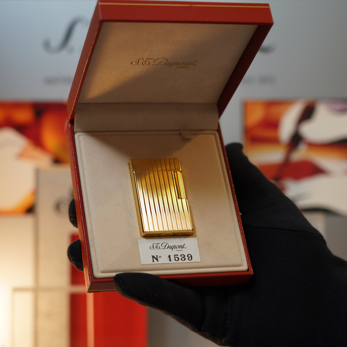A gloved hand holds an open red box displaying a Vintage November 1987 S.T. Dupont Large Ligne 1 Heavy rare pattern 18k Gold Finish Lighter by Lucy Lighter, serial number 1589 shown inside the lid.