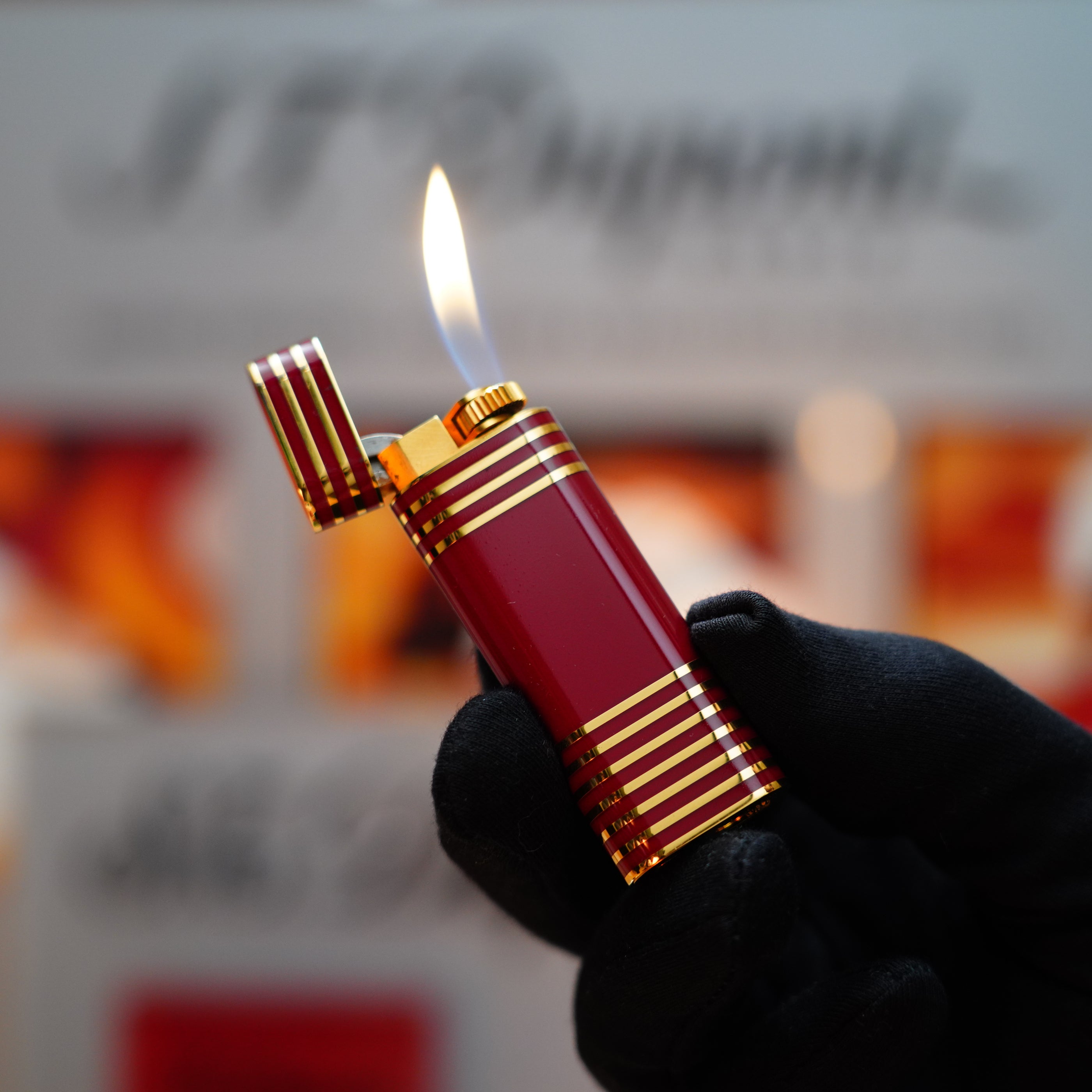 A gloved hand holds an open Vintage 1985 Cartier Burgundy Red 24k Gold Lacquer Le Must Lighter, showcasing its rare horizontal line design, red and 24k gold accents, and a lit flame.