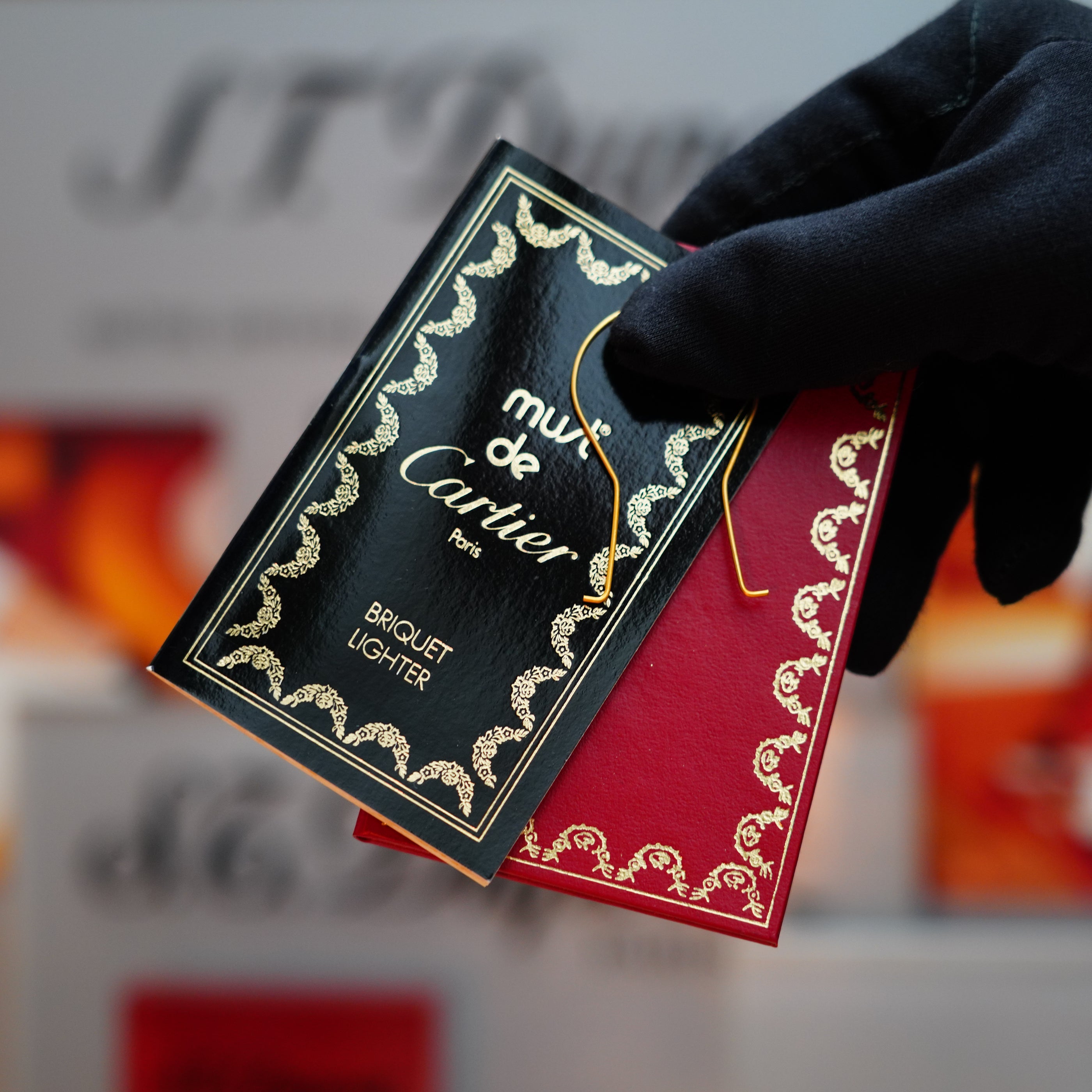 A gloved hand holds a burgundy red Cartier box with gold detailing, presenting the rare horizontal line pattern of a vintage 1985 Cartier 24k Gold Lacquer Le Must Lighter.