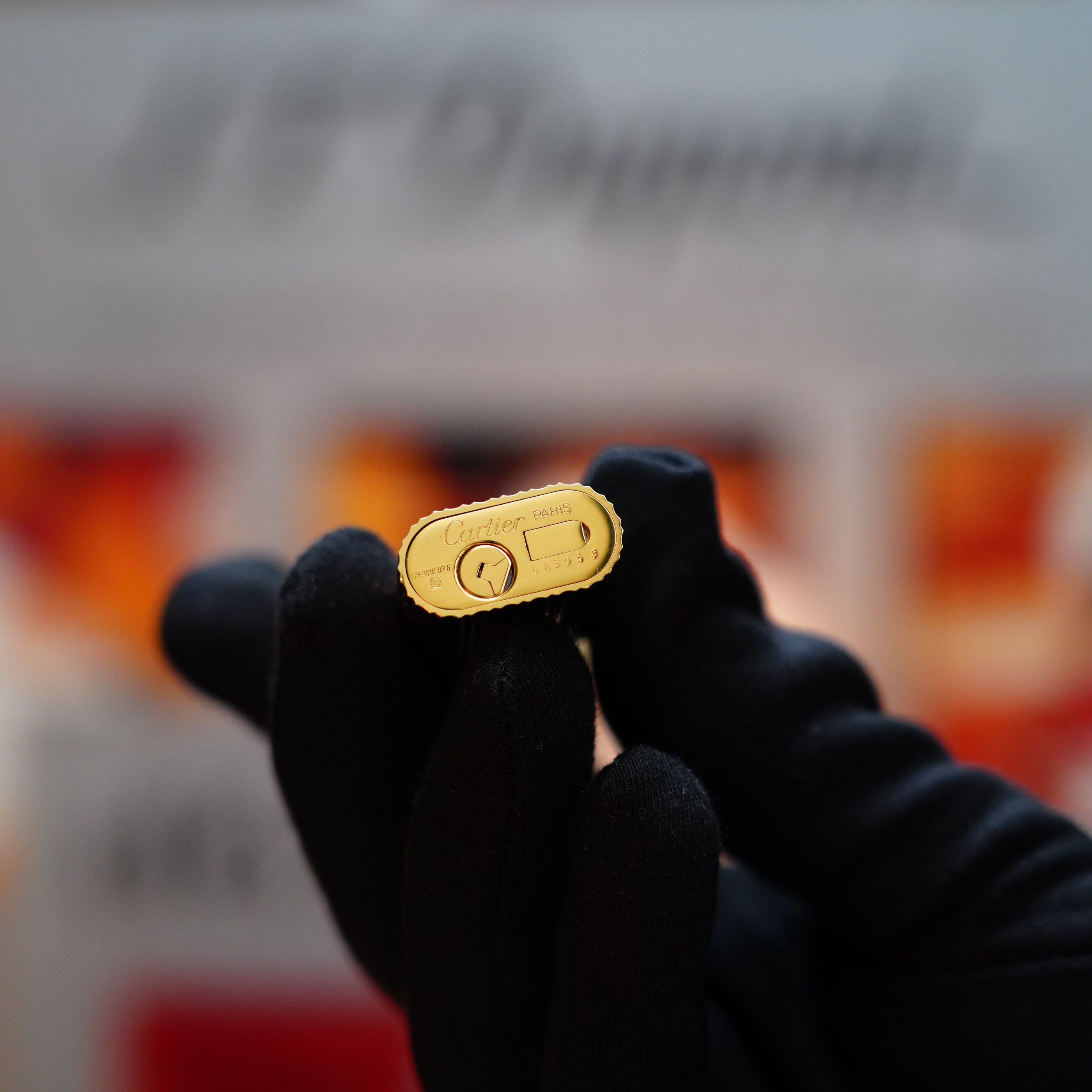 A person wearing black gloves holds a vintage 1980 Cartier 24k Gold Finish Double Vertical Line Le Must Lighter, a true collector's item, against a blurred background.