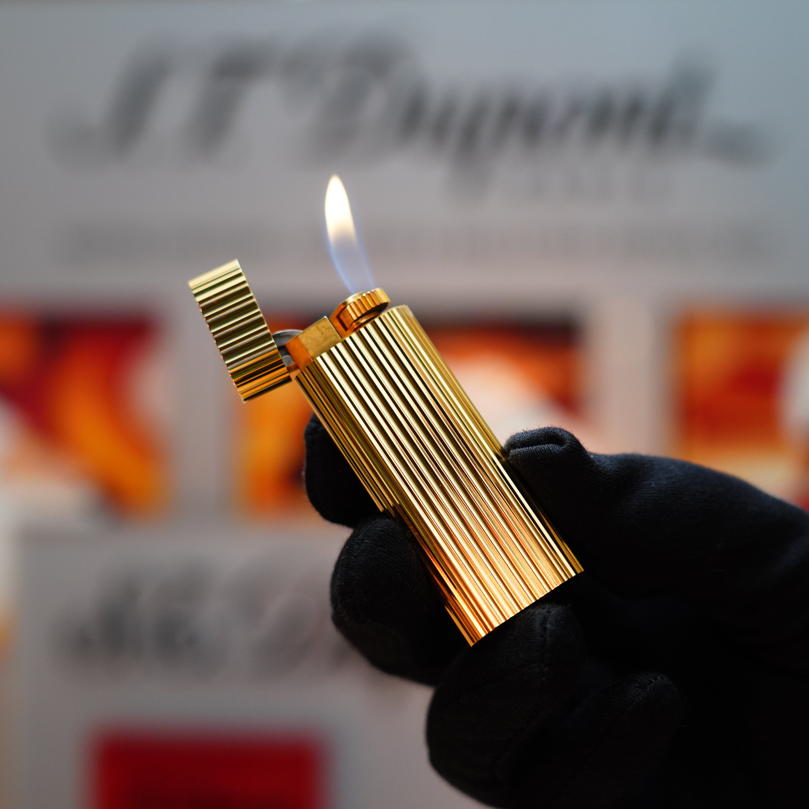 A gloved hand holding a sophisticated Vintage 1980 Cartier 24k Gold Finish Double Vertical Line Le Must Lighter with a visible flame, highlighting its ribbed design and enduring elegance—a genuine collector's treasure.