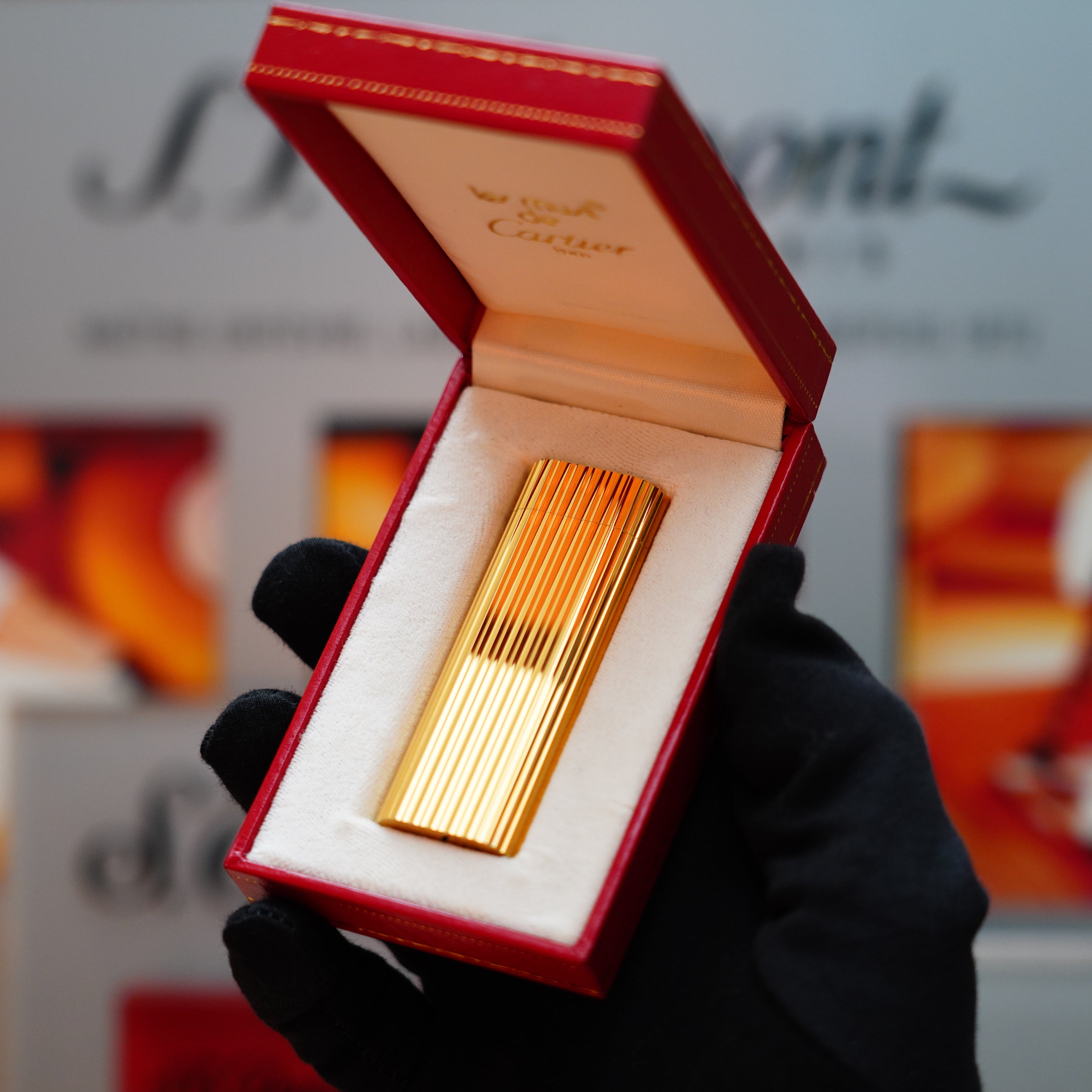 A person in black gloves holds an elegant Vintage 1980 Cartier 24k Gold Finish Double Vertical Line Le Must Lighter, reminiscent of a Collector's Item, nestled in a red velvet-lined box.