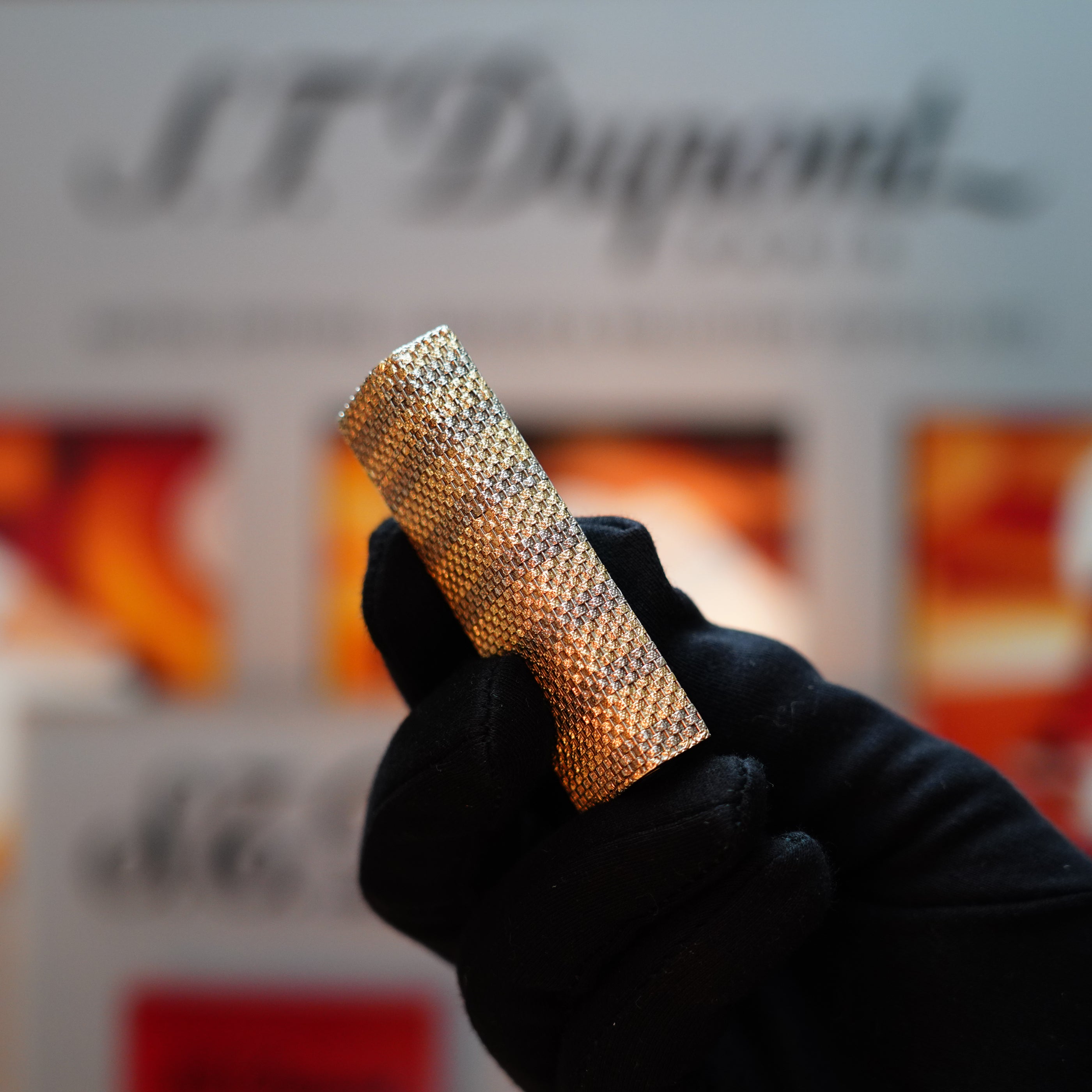 A gloved hand holds a textured, cylindrical metallic object—a Vintage 1978 Cartier Rare Pentagon Solid 18k Gold Jacket Basket Lighter with 750 hallmarks—against a blurred background with text.