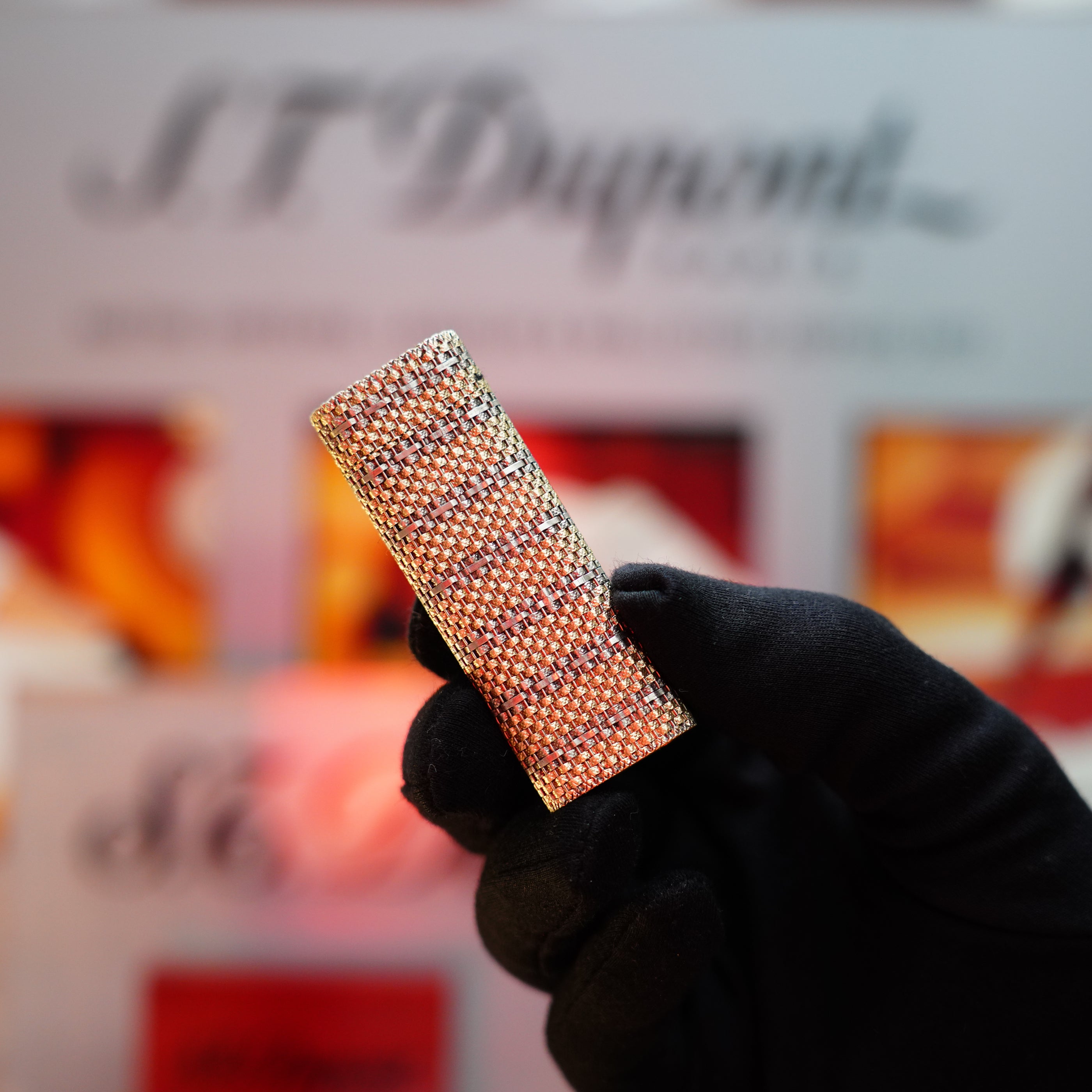 A gloved hand holding a rare collectible, solid 18k gold, diamond-encrusted lighter shimmers against a blurred background displaying the brand name "Cartier," specifically showcasing the Vintage 1982 Cartier Solid 18k Gold Jacket Basket with 750 hallmarks Lighter.