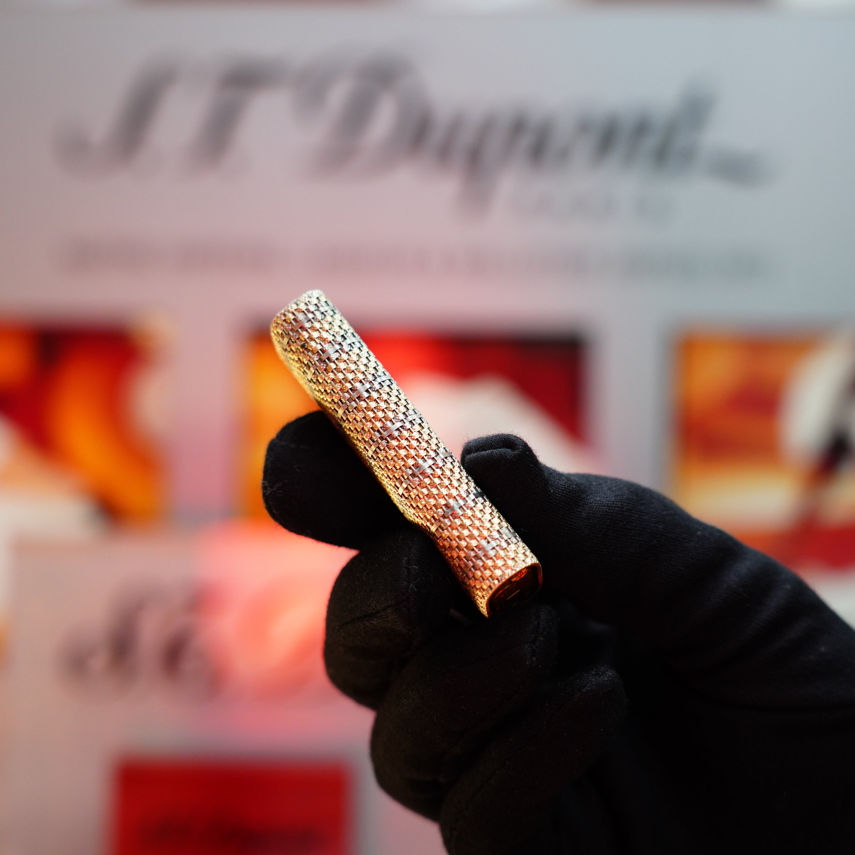 A gloved hand holds a lavish lighter, the Vintage 1982 Cartier Solid 18k Gold Jacket Basket adorned with 750 hallmarks, set against a blurred background featuring the Cartier logo.