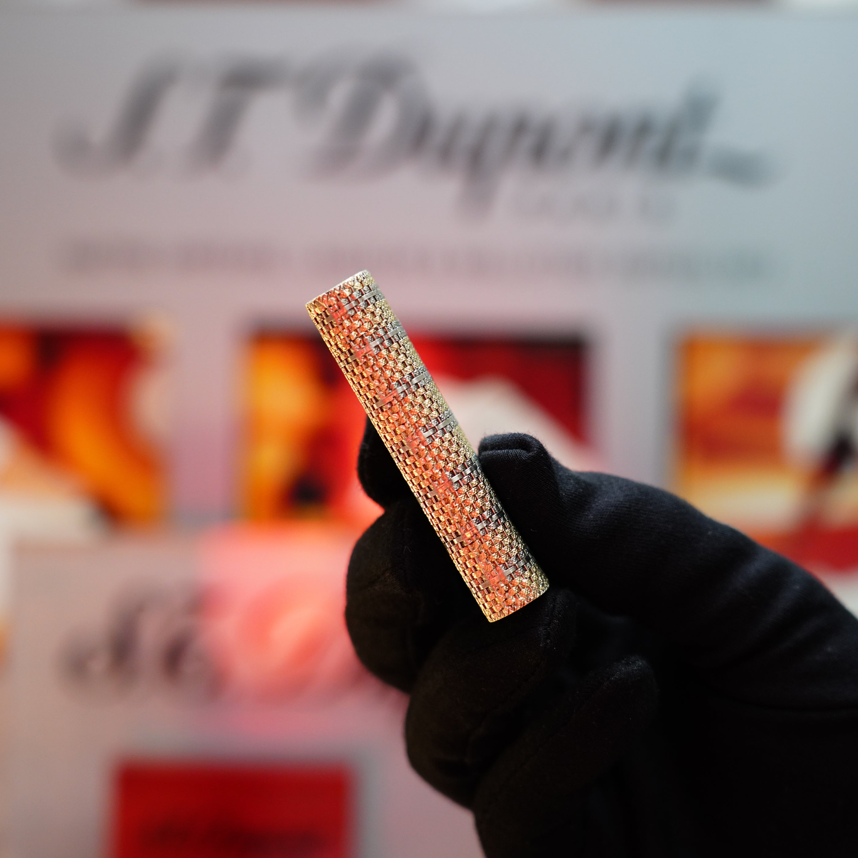 A gloved hand holds a rectangular, jewel-encrusted Vintage 1982 Cartier Solid 18k Gold Jacket Basket lighter with blurred signage in the background.