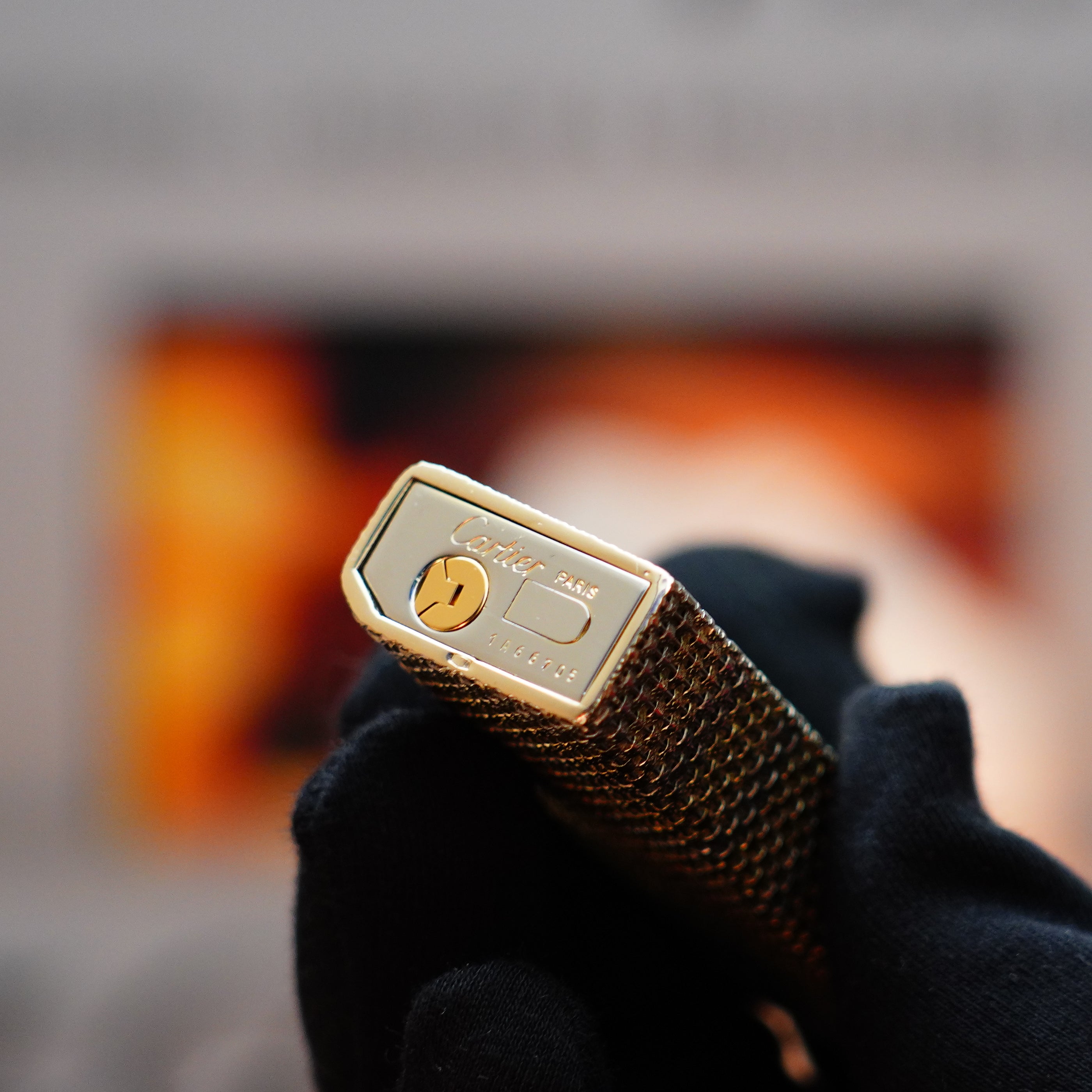 A gloved hand holds a rare 1978 Cartier Pentagon lighter, its solid 18k gold jacket basket design gleaming with vintage elegance, reminiscent of the craftsmanship found in premium Parisian creations.