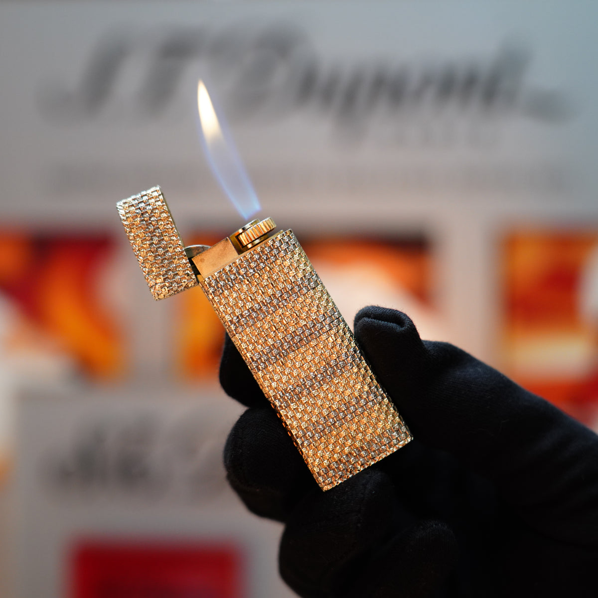 A gloved hand holds a lit, vintage 1978 Cartier Pentagon lighter from the rare Basket Series, crafted in solid 18k gold with 750 hallmarks, shining against a blurred background.