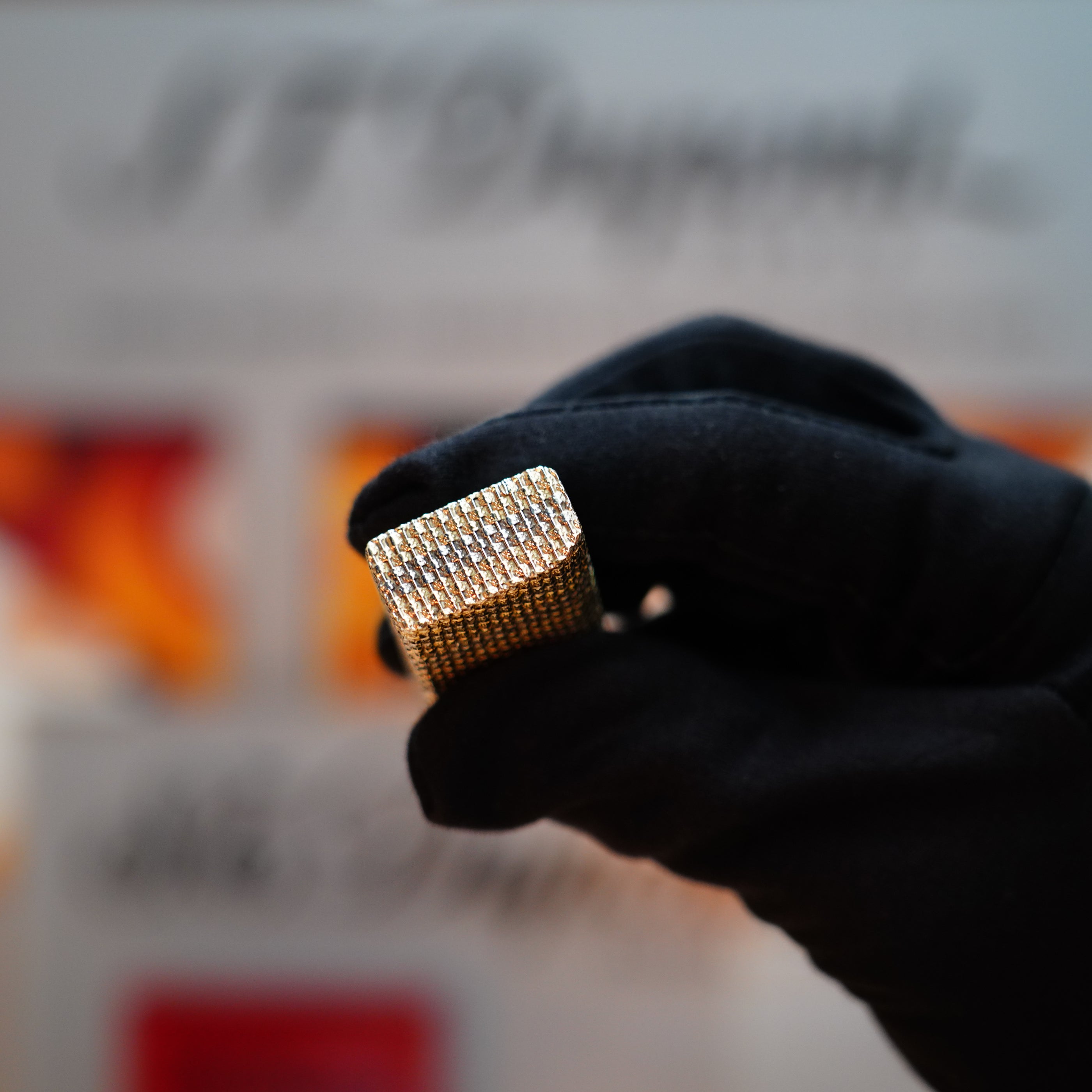 A gloved hand holds the Vintage 1978 Cartier Rare Pentagon Solid 18k Gold Jacket Basket lighter, its gold-toned form gleaming against a blurred background.