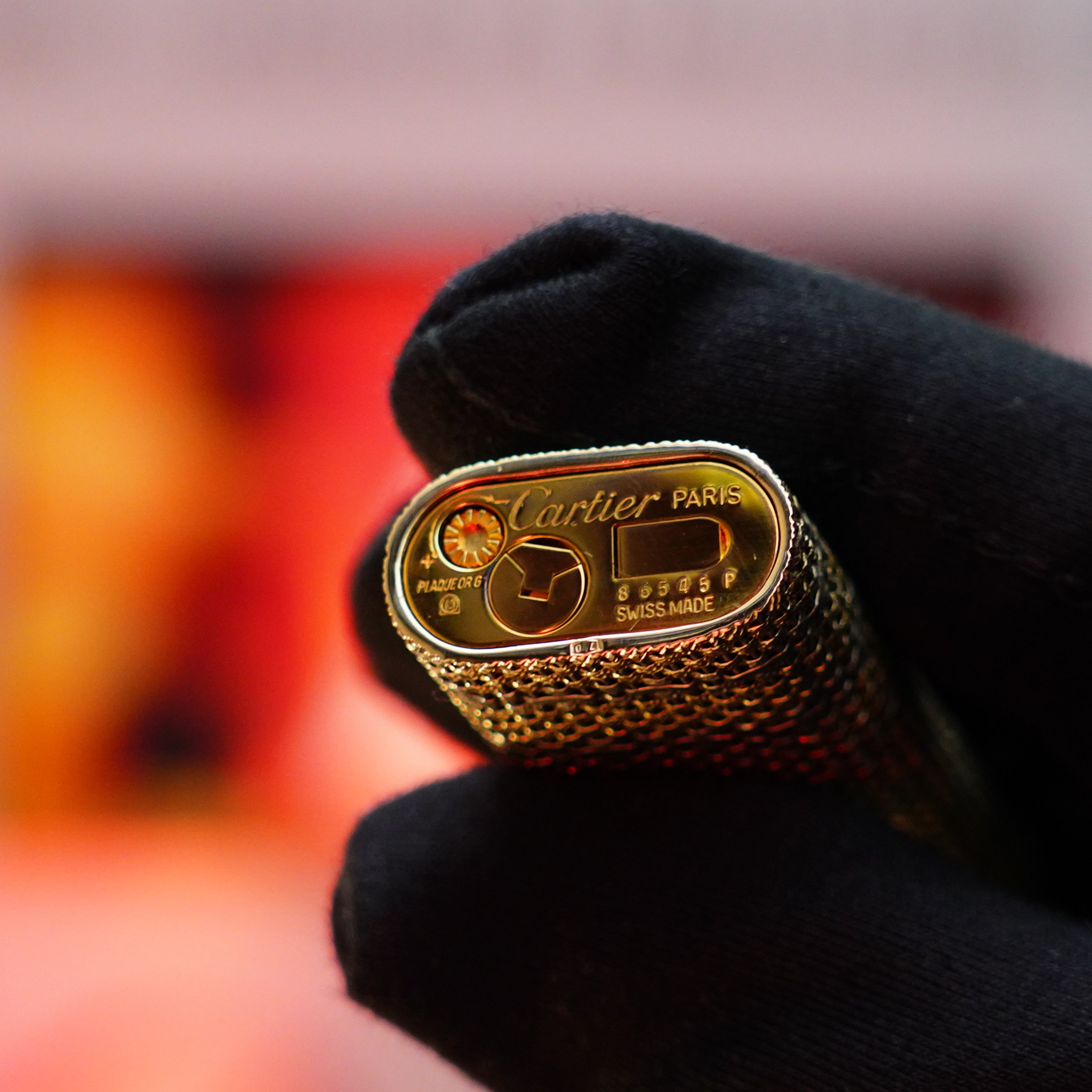 A gloved hand holds a valuable collectible, the Vintage 1982 Cartier Solid 18k Gold Jacket Basket Lighter featuring 750 hallmarks, inscribed with "Paris" and "Swiss Made," along with its serial numbers.