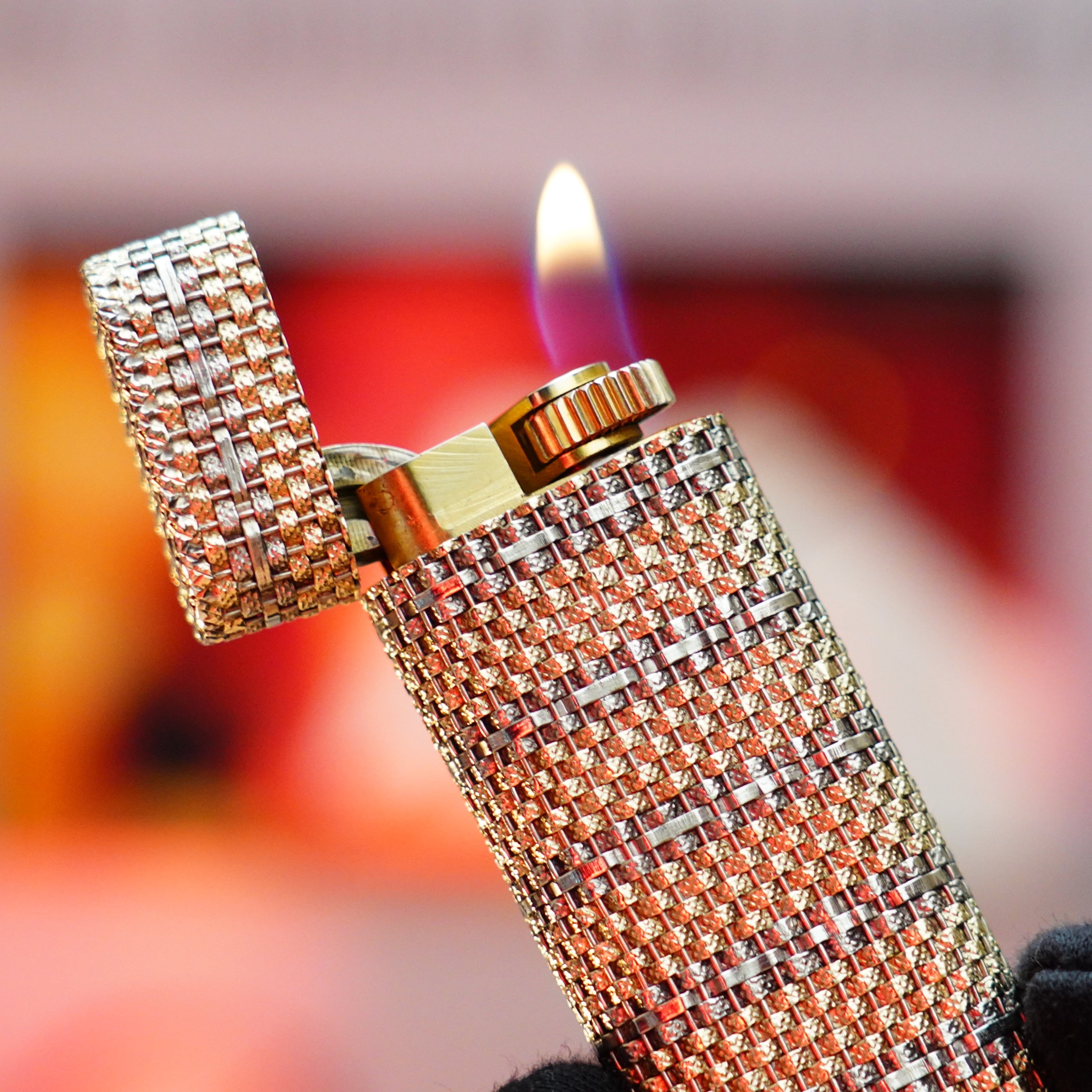 A close-up of a rare collectible reveals a Vintage 1982 Cartier Solid 18k Gold Jacket Basket lighter, adorned with intricate patterns and featuring 750 hallmarks in silver and gold, with its lid open and a small flame lit.