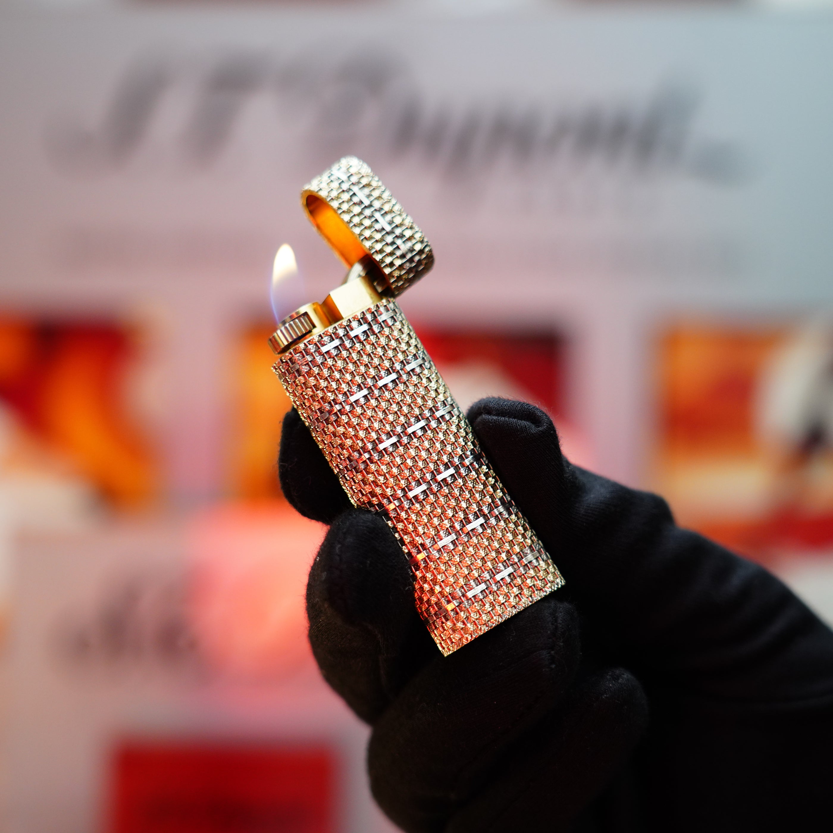 A gloved hand holds an ornate, diamond-encrusted Vintage 1982 Cartier Solid 18k Gold Jacket Basket with 750 hallmarks lighter, igniting a flame against a blurred background.